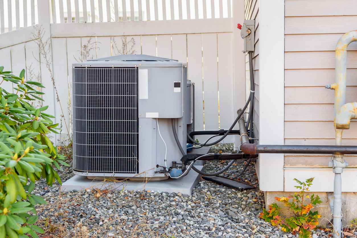HVAC system external unit by a wooden fence in a house backyard.