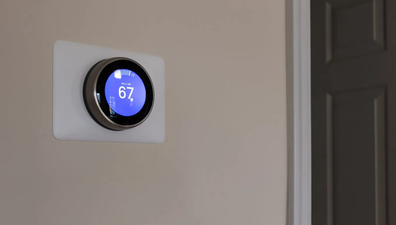 Smart thermostat on the wall of a home displaying 67 degrees.